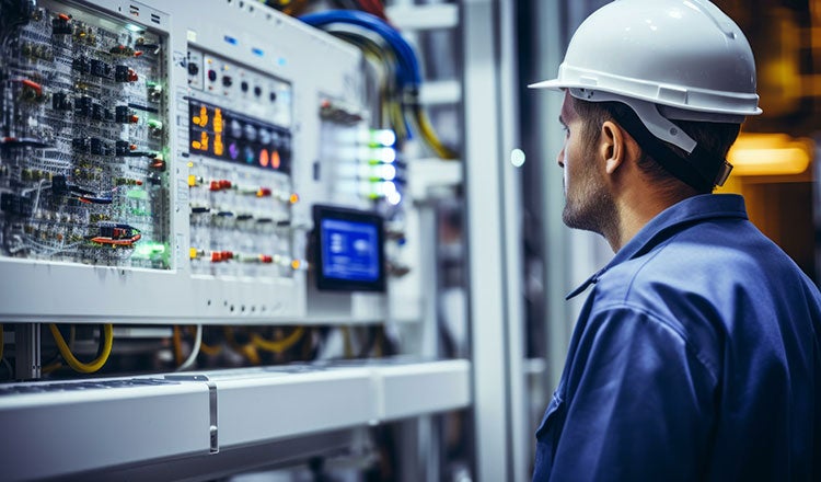 Electrical Engineer in a safety hat looking at a switchboard.