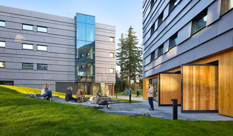 People attending an outdoor class on a college campus, surrounded by newly constructed buildings